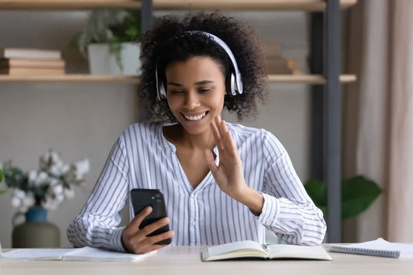 Young black woman in headphones wave hand to phone — Stock Photo, Image