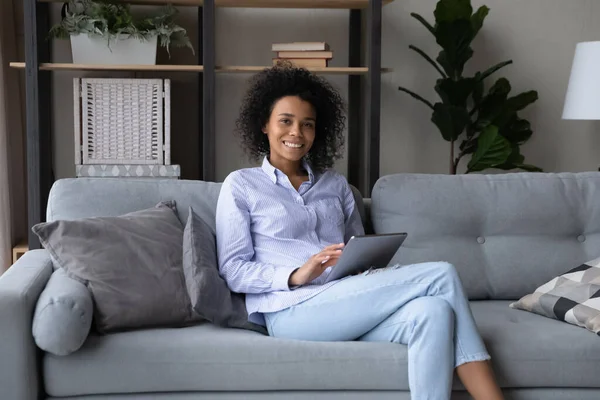 Retrato de una joven hembra negra sentada en un sofá sosteniendo una tableta — Foto de Stock