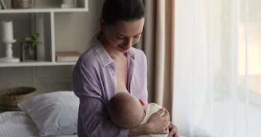 Genç anne yeni doğmuş bebeği emziriyor. Evde yatakta oturuyor.