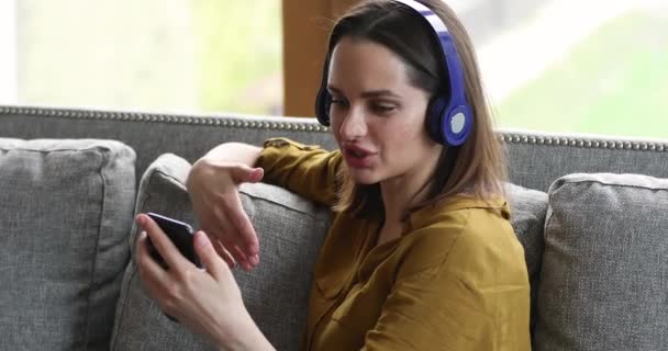 女性はスマートフォンを使ってヘッドフォンを着用してビデオ通話に参加します — ストック動画