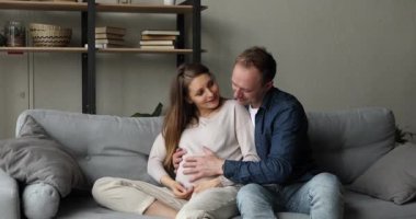 Hamile kadın, şefkatli kocası kameraya bakıp gülümsüyor.