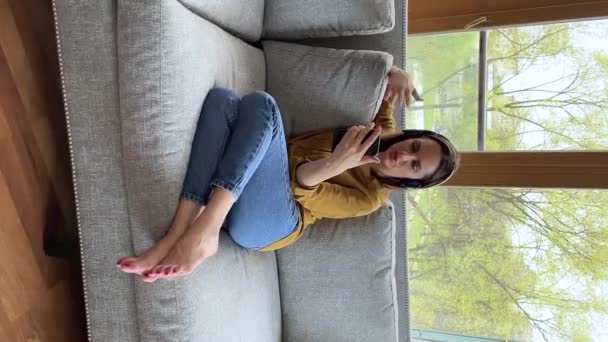 Женщина в наушниках наслаждается удаленным разговором по мобильному телефону через видеокамеру — стоковое видео