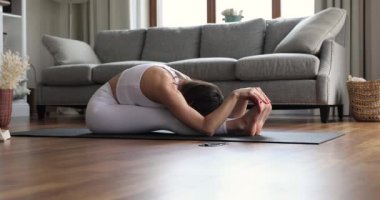 Önde mindere oturmuş yoga yapan genç bir kadın.