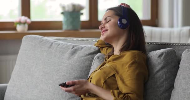 Mulher relaxante interior detém celular desfrutar de som de qualidade através de fones de ouvido — Vídeo de Stock