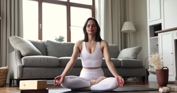 Mujer meditando sentada con las piernas cruzadas en la esterilla de yoga en casa — Vídeos de Stock