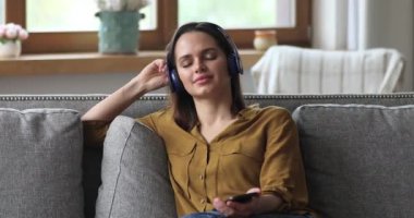 Kadın en sevdiği müziği telsiz kulaklıkla akıllı telefondan dinliyor.