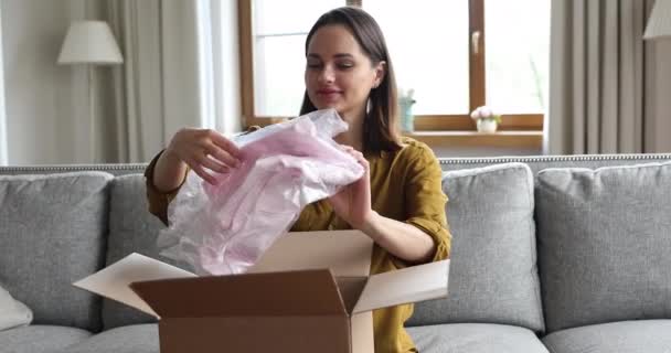 Молодая женщина открыла коробку с посылками, распаковала доставленную одежду онлайн — стоковое видео