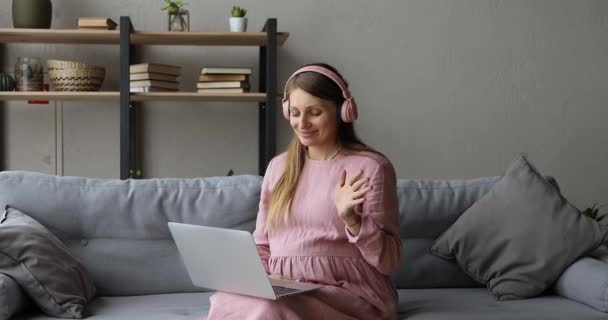 Wanita hamil di headphone duduk di sofa membuat panggilan video — Stok Video