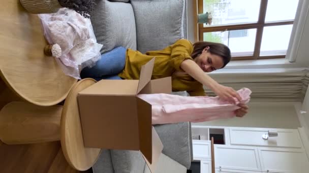 Vista vertical de la mujer que revisa la caja de paquetes recibida con ropa de dama — Vídeo de stock