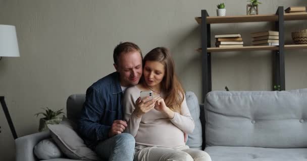 Loving man knuffels zwangere vrouw met behulp van smartphone kopen op internet — Stockvideo