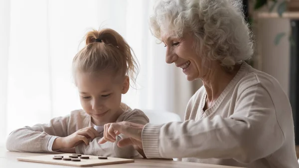 Cheerful curious small girl learning playing checkers with granny. — Stock Photo, Image