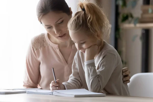 Pozorný mladý matka pomáhá malé dítě dcera s domácím úkolem. — Stock fotografie