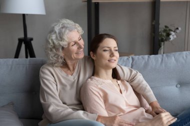 Sevecen orta yaşlı bir anne ve yetişkin bir kızı kanepede dinleniyor..