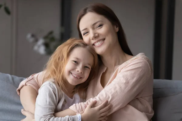 Retrato de una joven cariñosa abrazando a su pequeña hija sonriente. —  Fotos de Stock