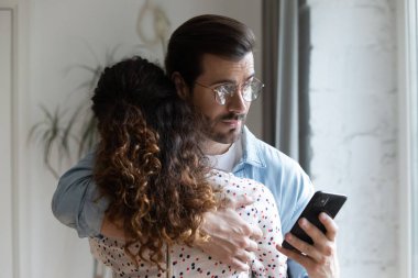 Kıskanç koca karısına sarılıyor ve telefonunu kontrol ediyor.