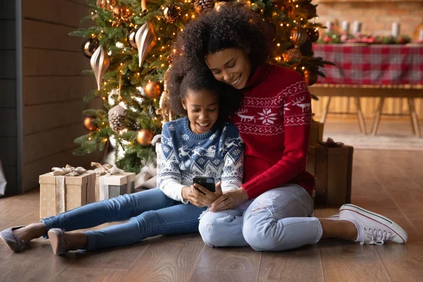 Happy biracial mom and daughter use cellphone on Christmas