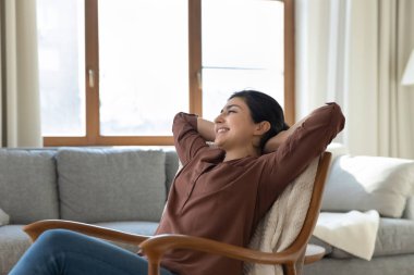Huzurlu genç Hintli kadın oturma odasında koltukta dinleniyor.