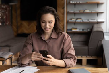 Mutlu kadın masada oturup internetten cep telefonu mesajı kullanıyor.