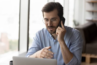 Kafkasyalı işadamı bilgisayar başında çalışıyor. Akıllı telefondan konuşuyor.