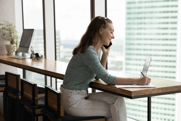 Empregada sorridente do sexo feminino trabalha em conversa de laptop no celular — Fotografia de Stock