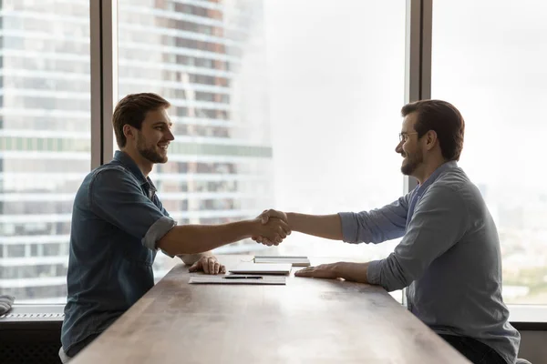 Smiling male employees handshake close deal at meeting