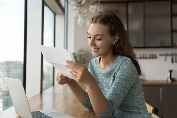 Leende kvinna arbete på laptop läsa goda nyheter i pappersarbete — Stockfoto