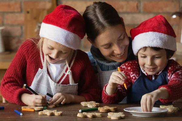 Jovem mãe decorando pães de gengibre de Natal com crianças pequenas. — Fotografia de Stock