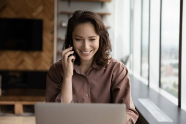Gülümseyen genç kadın dizüstü bilgisayarda çalışıyor cep telefonuyla konuşuyor