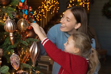 Mutlu genç anne küçük kızının Noel ağacını süslemesine yardım ediyor..