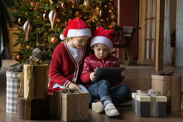 Crianças pequenas felizes em chapéus de Papai Noel usando tablet digital. — Fotografia de Stock