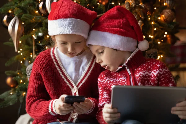 Menino e menina irmãos felizes usando presentes de tecnologia de Natal. — Fotografia de Stock