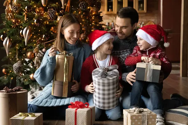 Sorrindo casal jovem família desembrulhando presentes de Natal com crianças. — Fotografia de Stock