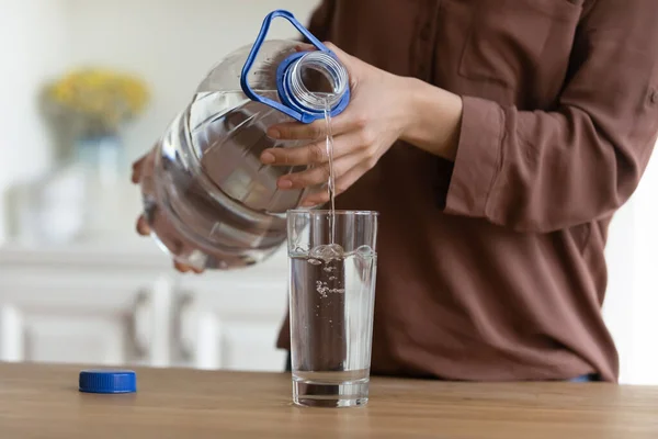 Las manos de mujer joven vierten agua en vidrio de la botella de plástico — Foto de Stock