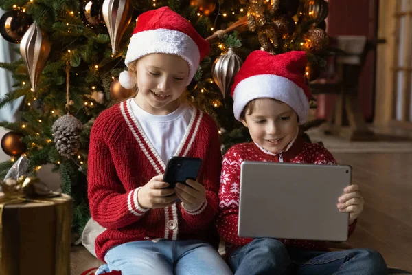 Małe szczęśliwe dzieci rodzeństwo za pomocą prezentów świątecznych elektroniczne gadżety. — Zdjęcie stockowe