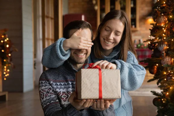 Szczęśliwa młoda kobieta daje prezent niespodzianka Boże Narodzenie dla męża. — Zdjęcie stockowe