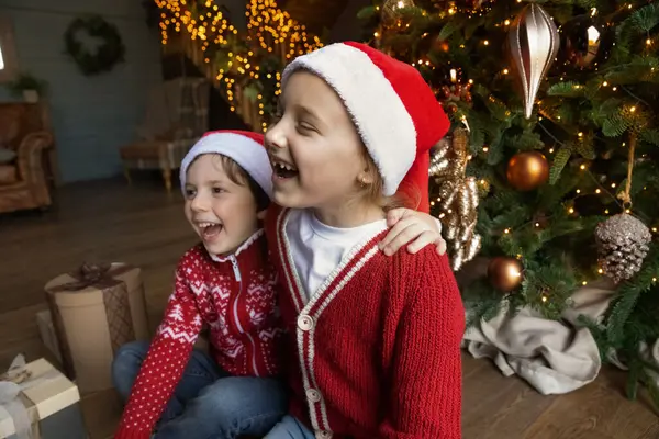 Crianças pequenas felizes se divertindo sentadas perto da árvore de Natal. — Fotografia de Stock