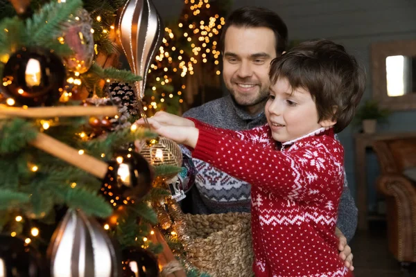 Glad ung man hjälpa lilla barn son dekorera julgran. — Stockfoto