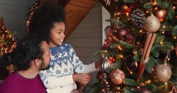 Lächelnde junge afrikanisch-amerikanische Familie schmückt Weihnachtsbaum. — Stockvideo