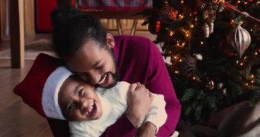 Neşeli Afrikalı etnik babası Noel ağacının yanında oğluyla oynuyor..