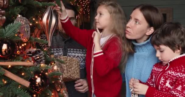 両親と一緒にクリスマスツリーを飾る幸せな小さな愛らしい子供たち. — ストック動画