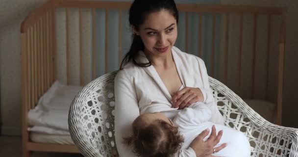 Jeune maman allaitant son bébé assis sur une chaise confortable intérieure — Video