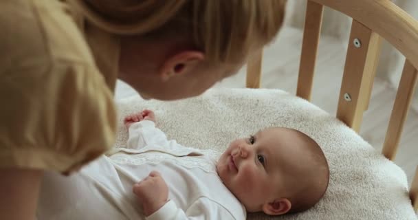 Loving mother amuse to baby lying on comfort crib — Stock Video