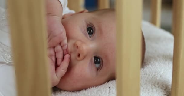 Väckt söt bebis liggande i babysäng med fingrar i munnen — Stockvideo