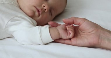 Anne, uyuyan yeni doğan bebeğin elini tutuyor, yakın çekim görüntüsü.