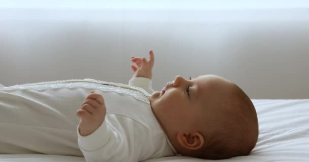 Закройте симпатичного новорожденного ребенка в телесном костюме лежащего на кровати — стоковое видео