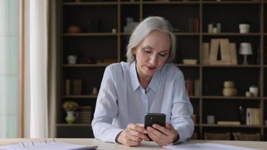 Masada oturan olgun kadın cep telefonundan iyi haberler okuyor.