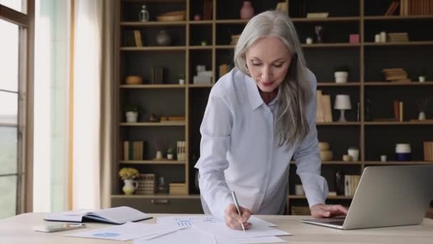 Ältere Geschäftsfrau beschäftigt sich mit Präsentationserstellung, nutzt Laptop, erledigt Papierkram — Stockvideo