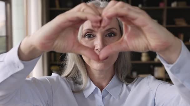 Cara de mujer mayor mirando a través de los dedos unidos mostrando la forma del corazón — Vídeo de stock