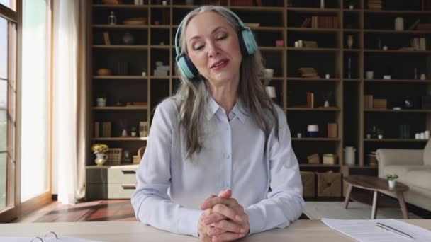 Ältere Frau mit Kopfhörer blickt in Kamera und spricht — Stockvideo