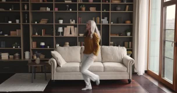 Літня жінка в повсякденному одязі танцює сама у вітальні — стокове відео